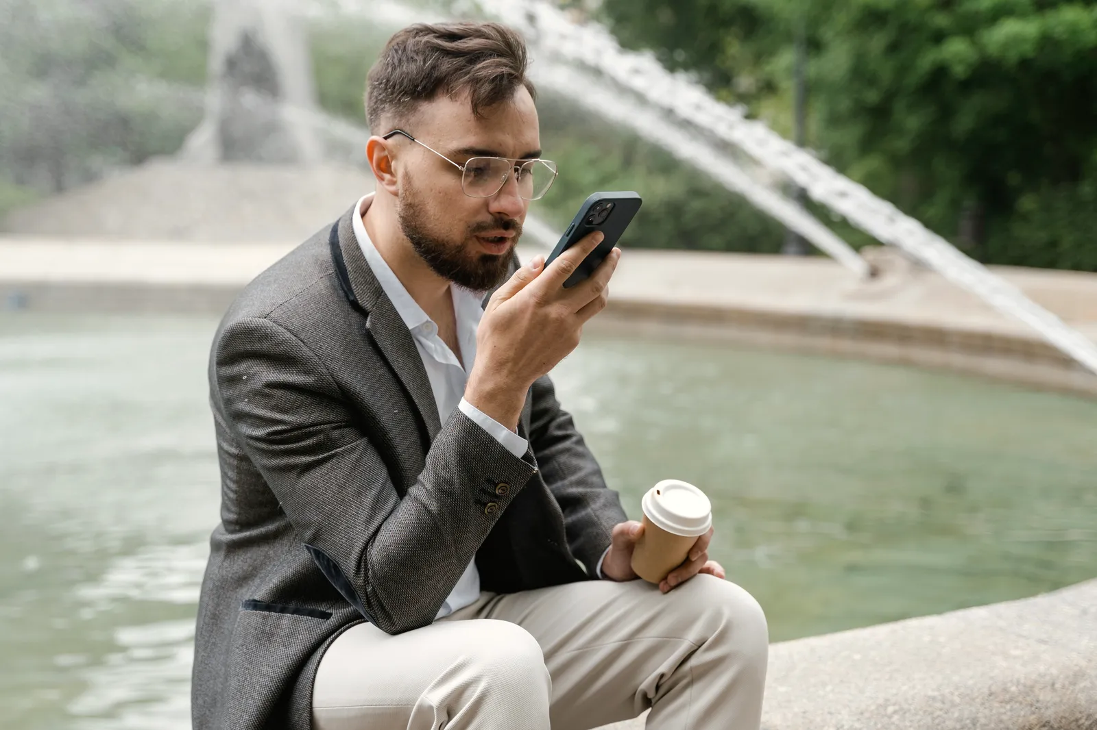 Ein Mann im Sakko spricht draußen nach einem Termin eine Sprachnotiz in sein Smartphone